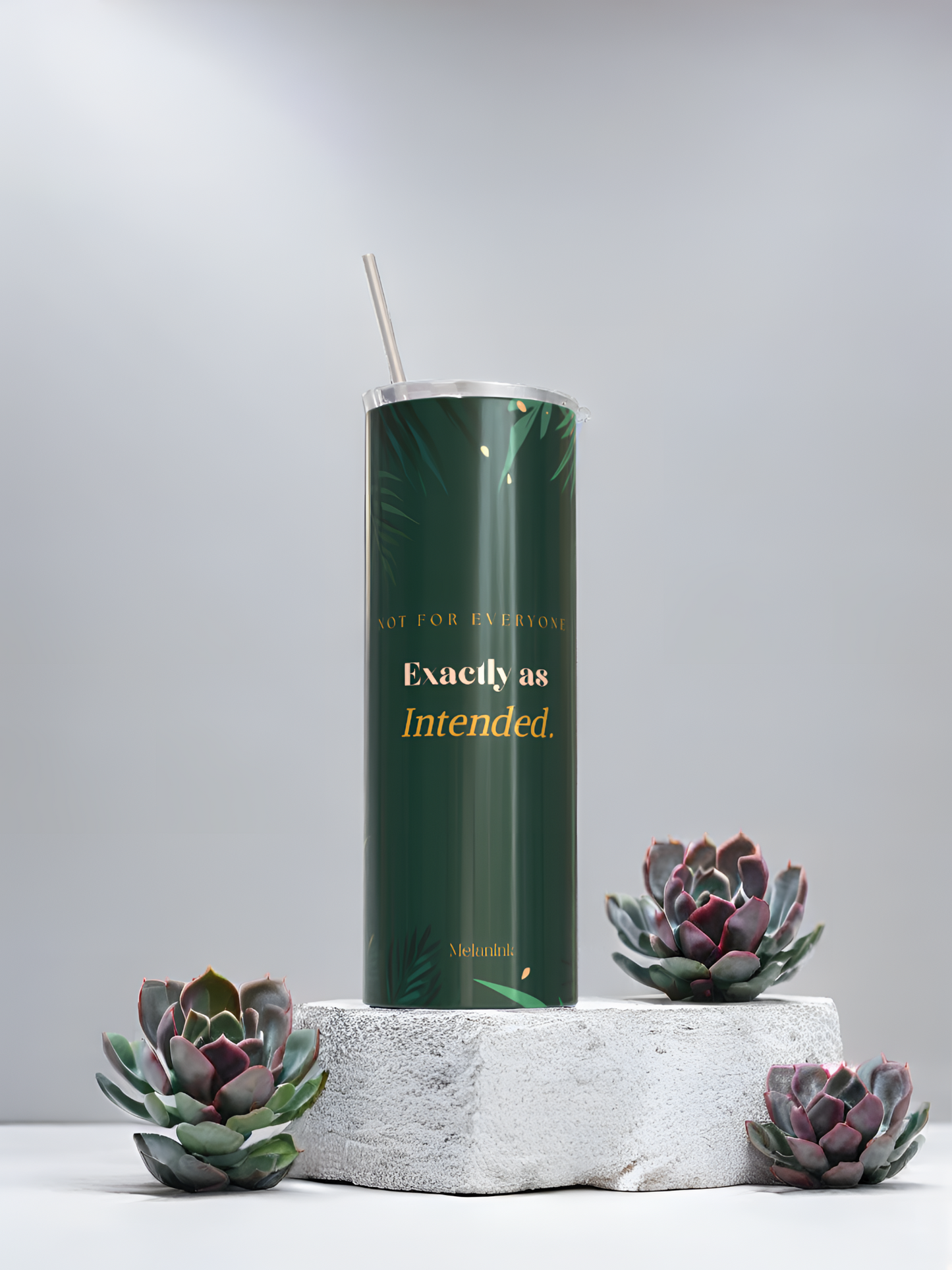 MelanInk Designs Emerald Garden 20oz sublimation tumbler from the Bloom & Dusk Collection. Deep emerald green wrap design with gold botanical palm leaf detail and layered gold typography. Displayed on a white textured stone pedestal with green and purple succulent plants. Clean minimal grey background. Handcrafted and pressed to order in Atlanta Georgia. Black owned small business. Sublimation tumbler gift for her.