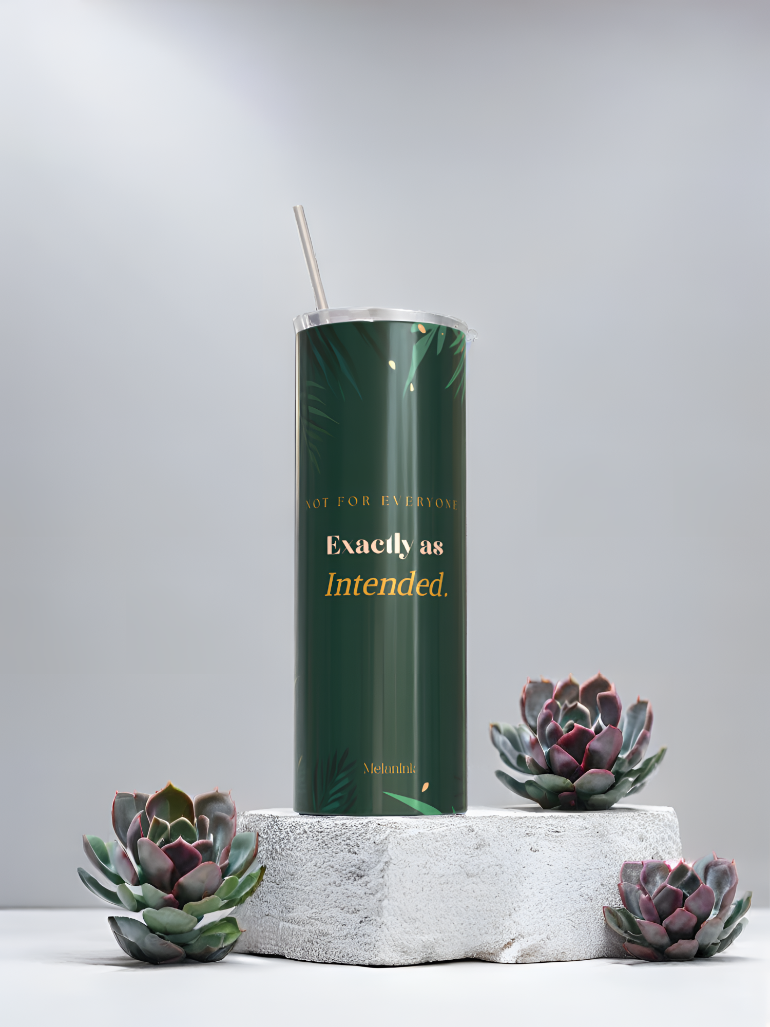 MelanInk Designs Emerald Garden 20oz sublimation tumbler from the Bloom & Dusk Collection. Deep emerald green wrap design with gold botanical palm leaf detail and layered gold typography. Displayed on a white textured stone pedestal with green and purple succulent plants. Clean minimal grey background. Handcrafted and pressed to order in Atlanta Georgia. Black owned small business. Sublimation tumbler gift for her.